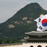 Economic value: Picture of the flag of South (the Republic of) Korea with a building and hill in the background,