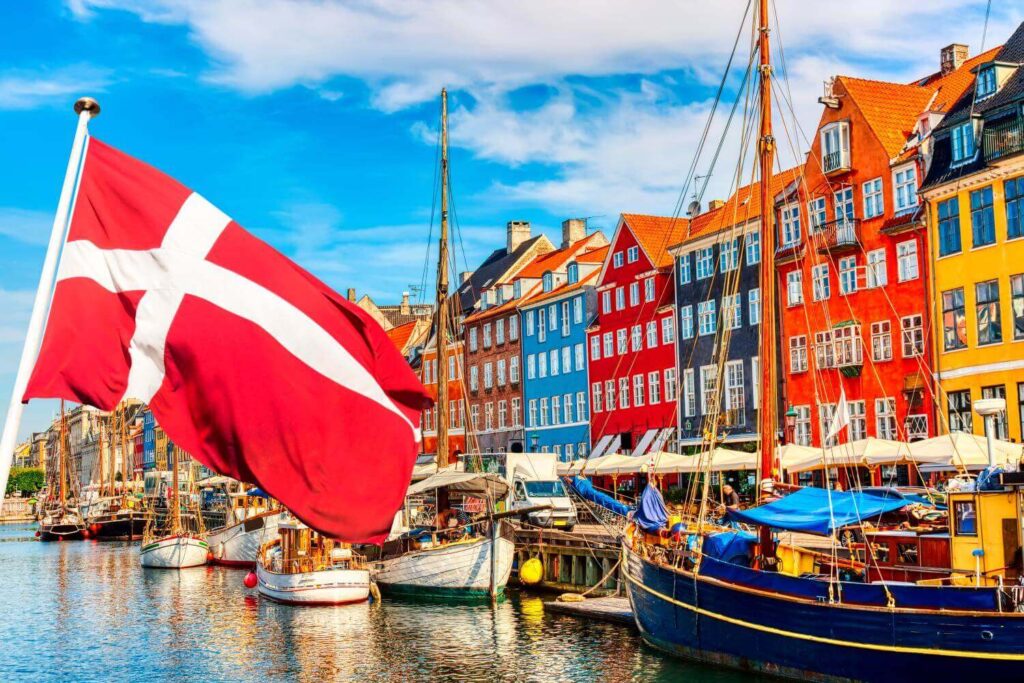 Political development: Picture of Danish flag in front of a number of boats in front of a number of brightly colored row houses